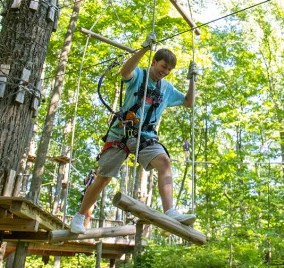 Young man navigating a suspended rope obstacle at TreEscape Aerial Adventure Park in Vernon, NJ, surrounded by trees and enjoying the thrill of outdoor adventure.