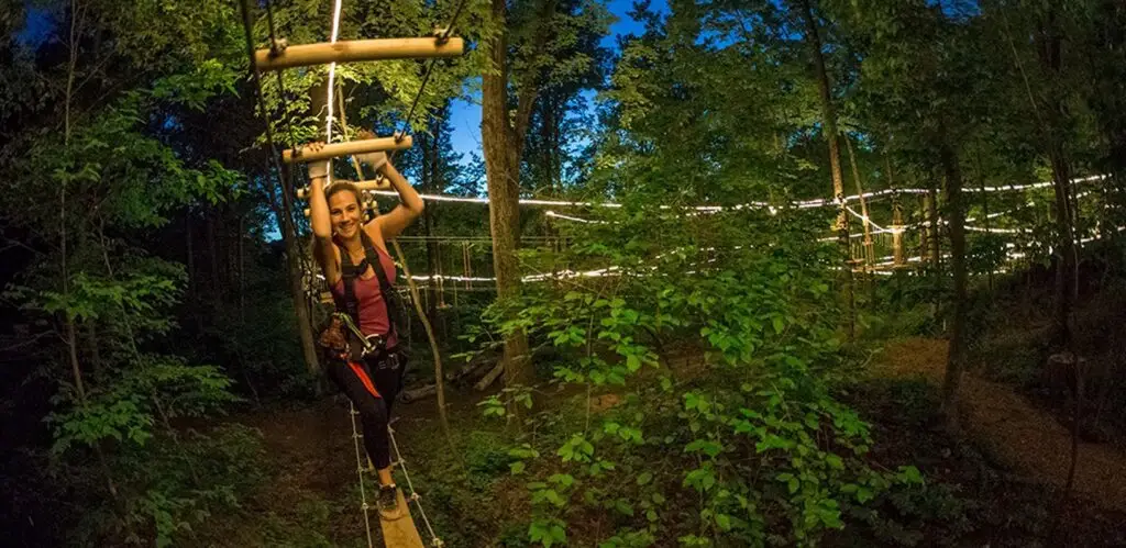 Young woman seen from the side participating in an outdoor nocturnal ropes course activity at TreEscape Aerial Adventure Park in Vernon, NJ.