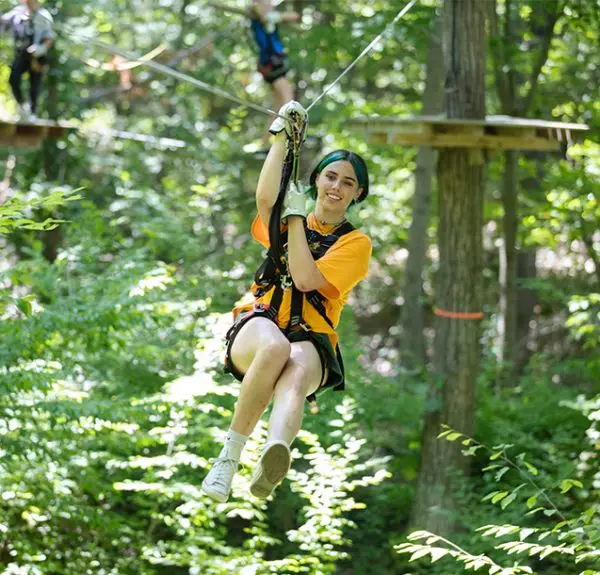 Young woman zip lining through the trees at TreEscape Aerial Adventure Park in Vernon, NJ, enjoying an outdoor adventure at Great Gorge