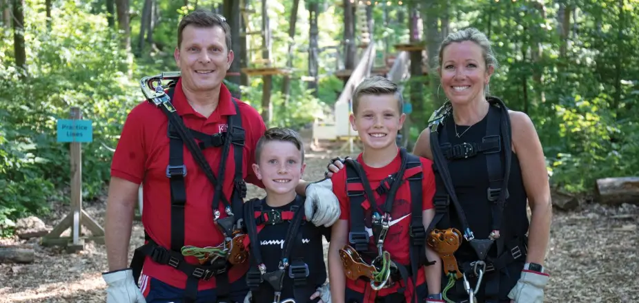 Smiling family enjoying outdoor activities together at TreEscape Aerial Adventure Park in Vernon, NJ, surrounded by trees and adventure elements.