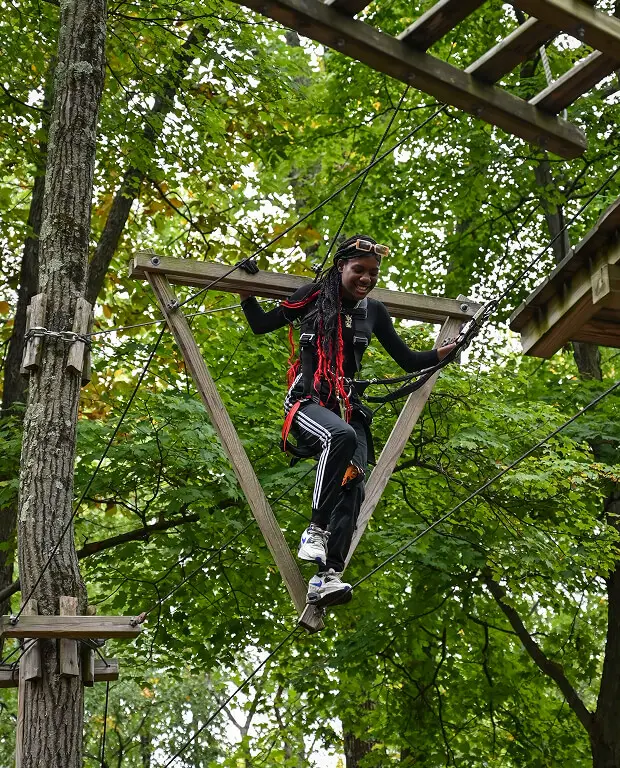 Woman taking part in a team-building activity at TreEscape Aerial Adventure Park in Vernon, NJ, engaging in a ropes course surrounded by trees.