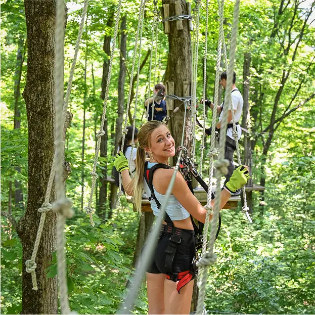 Group of young people navigating the aerial rope course at TreEscape Aerial Adventure Park in Vernon, NJ, working together and enjoying the forest adventure.