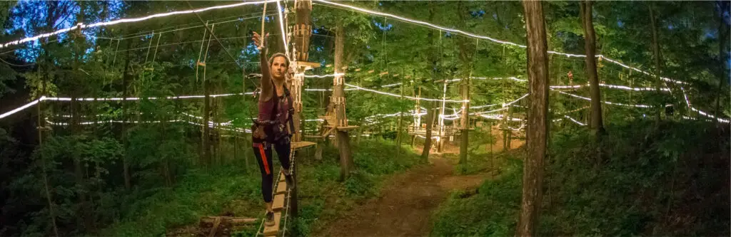 Woman at night climb at TreEscape Aerial Adventure Park in Vernon, NJ, working together and enjoying the forest adventure.