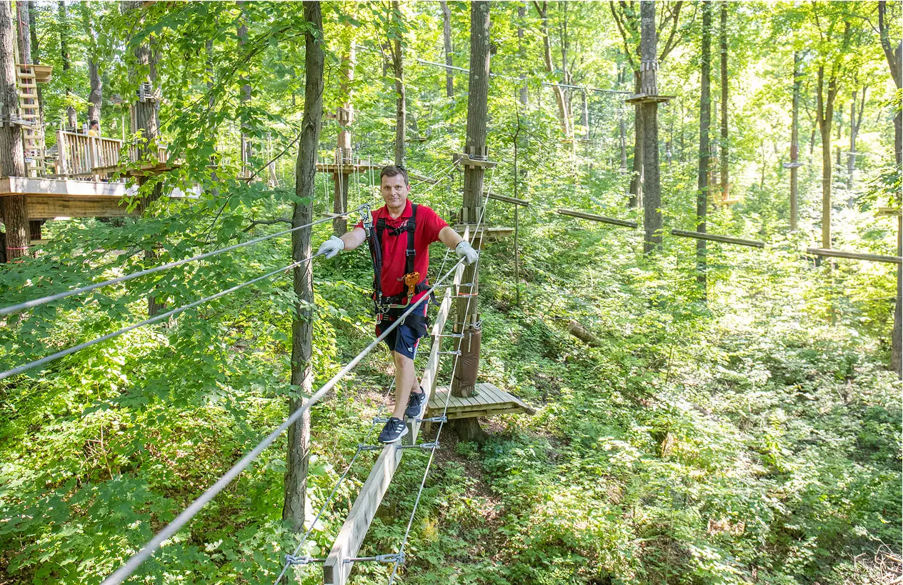 Young man confidently navigating the aerial ropes course at TreEscape Park in Vernon, NJ, tackling the challenge with focus and excitement high above the ground.