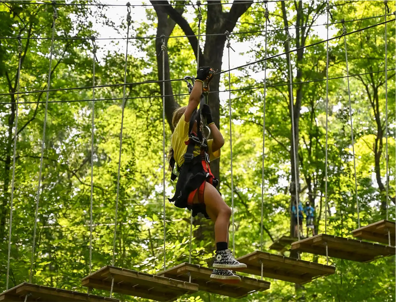 Kid confidently navigating the aerial ropes course at TreEscape Park in Vernon, NJ, enjoying the thrill of the challenge high above the ground.