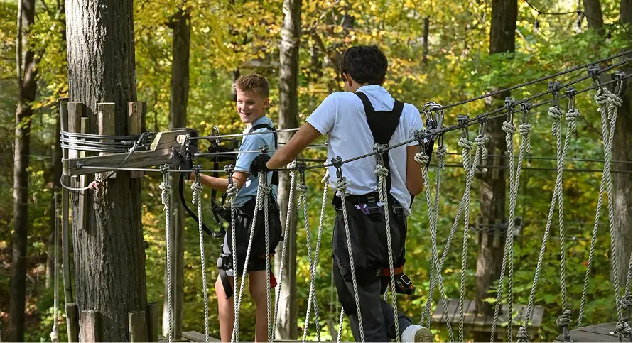 Two kids navigating the aerial rope course at TreEscape Park in Vernon, NJ, balancing and working together as they take on this exciting outdoor challenge.
