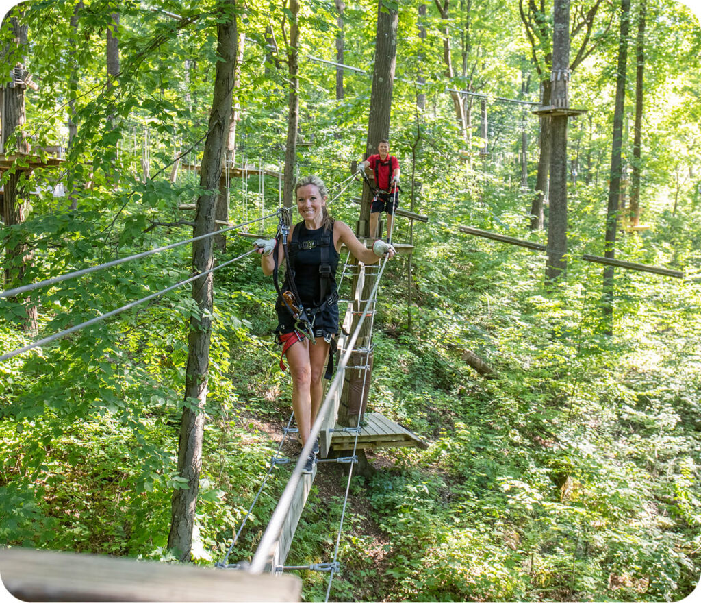 Woman expertly navigating the aerial ropes course at TreEscape Park in Vernon, NJ, embracing the challenge and enjoying the thrill of the outdoor adventure.