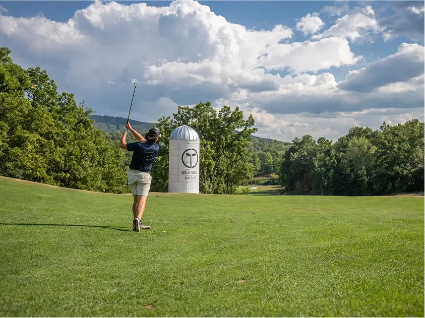 Man preparing to swing his golf club at a tee box at The Great Gorge Golf Club in Vernon, New Jersey, with scenic greenery in the background.