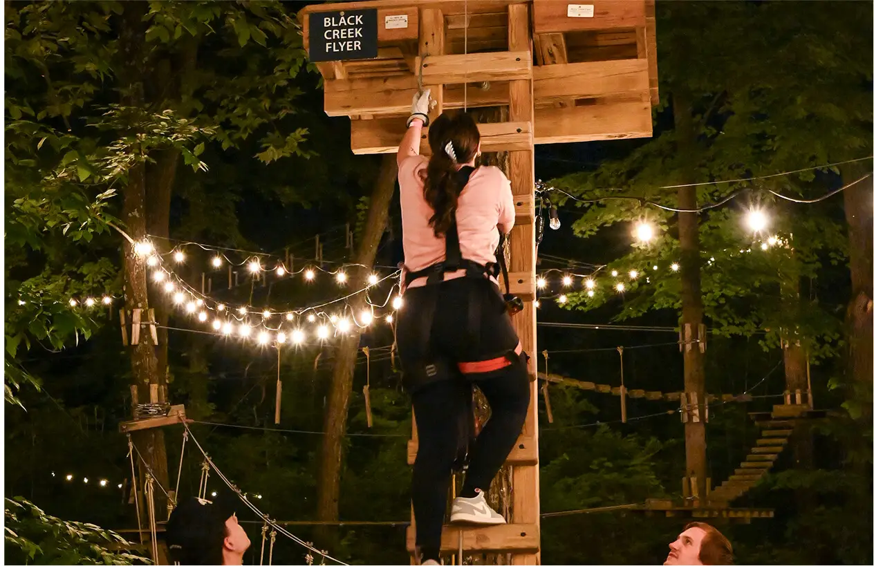 Group of young people at night climb at TreEscape Aerial Adventure Park in Vernon, NJ, working together and enjoying the forest adventure.