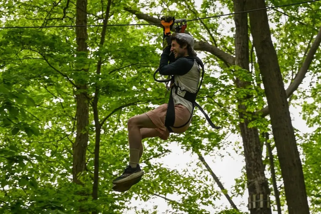 A man smiling while riding a zip line at TreEscape Aerial Adventure Park in Vernon, NJ, soaring through the trees with an exhilarating expression.