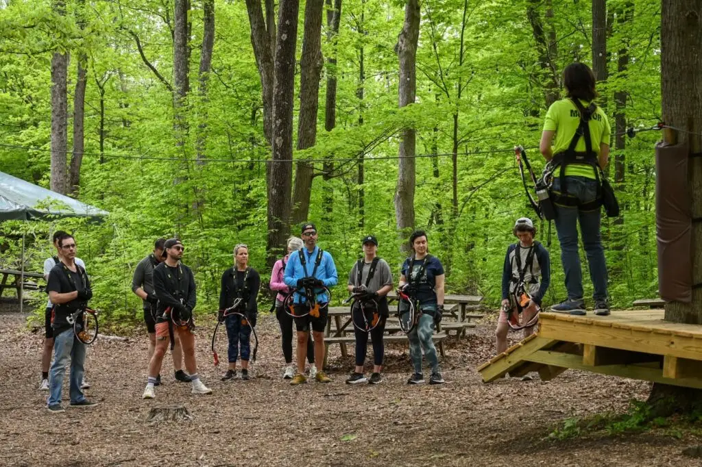 A group of people attentively listening to an instructor giving them instructions at TreEscape Aerial Adventure Park in Vernon, NJ, preparing for their ropes course adventure amidst the towering trees.